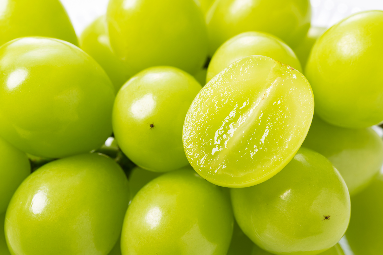 A lot of Shine-Muscat grapes and cut Shine-Muscat grapes on a wh